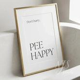 Minimal bathroom wall art featuring the quote “Don’t hurry, Pee Happy,” displayed in a slim gold frame beside a modern bathtub.