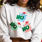 Woman wearing a white cropped sweatshirt with three colorful cute Santa characters spelling Ho Ho Ho.