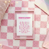 Pink educational poster in a pink frame laying on a pink and white checkered rug, perfect for preppy dorm decor.
