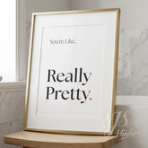 Bathroom wall art featuring the quote “You’re like, really pretty” in elegant serif typography with a small pink heart, displayed in a gold frame on a marble bathroom counter.