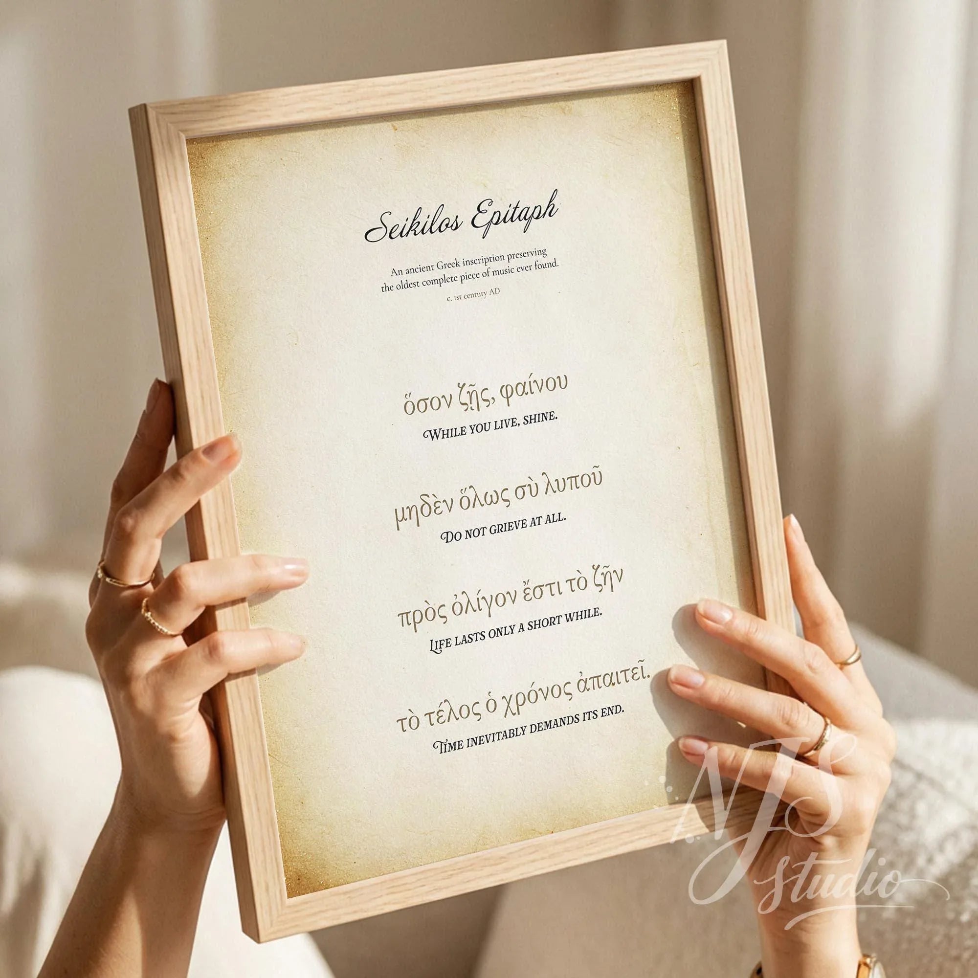 Hands holding a framed print with a vintage parchment background featuring the Seikilos Epitaph in Greek and English.