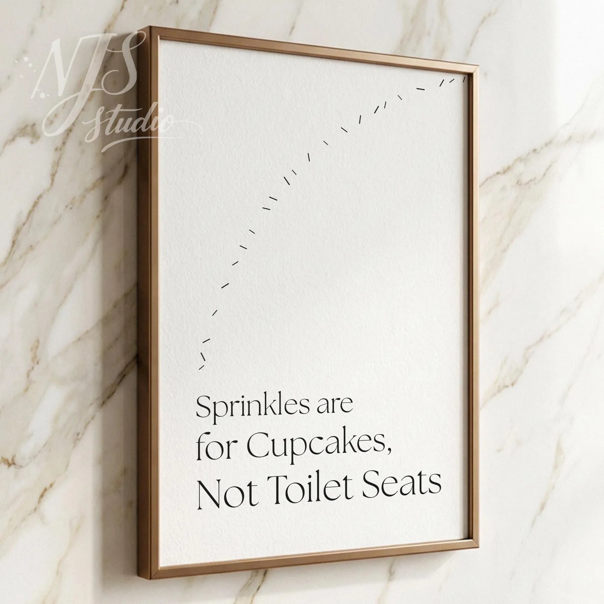 Minimal bathroom wall art featuring the quote “Sprinkles are for Cupcakes, Not Toilet Seats” in a light wood frame against marble tiles.