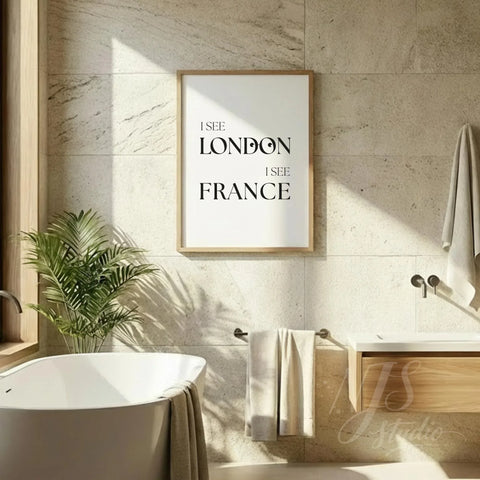 Humorous bathroom quote print reading “I See London I See France,” hung on a tiled wall above a bathtub in a bright spa-style bathroom.