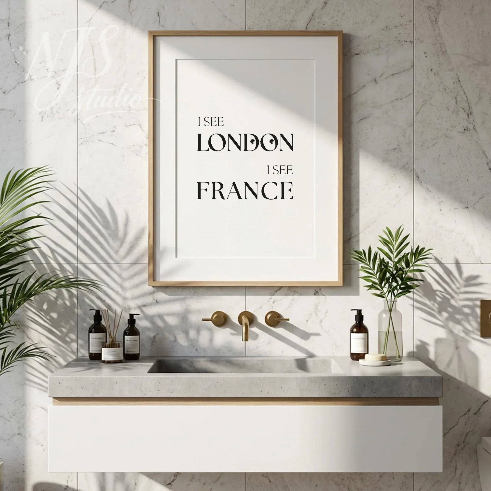 Humorous bathroom quote wall art reading “I See London I See France,” displayed above a modern vanity with plants and neutral decor.