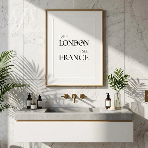 Humorous bathroom quote wall art reading “I See London I See France,” displayed above a modern vanity with plants and neutral decor.