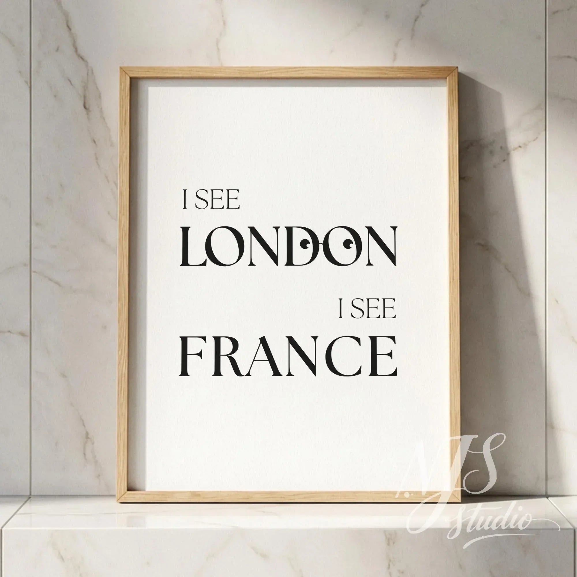 Minimal typography bathroom poster with the text “I See London I See France,” framed in natural wood and placed against a marble wall.