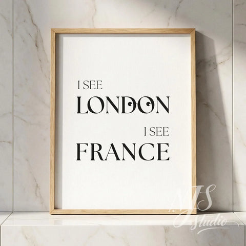 Minimal typography bathroom poster with the text “I See London I See France,” framed in natural wood and placed against a marble wall.