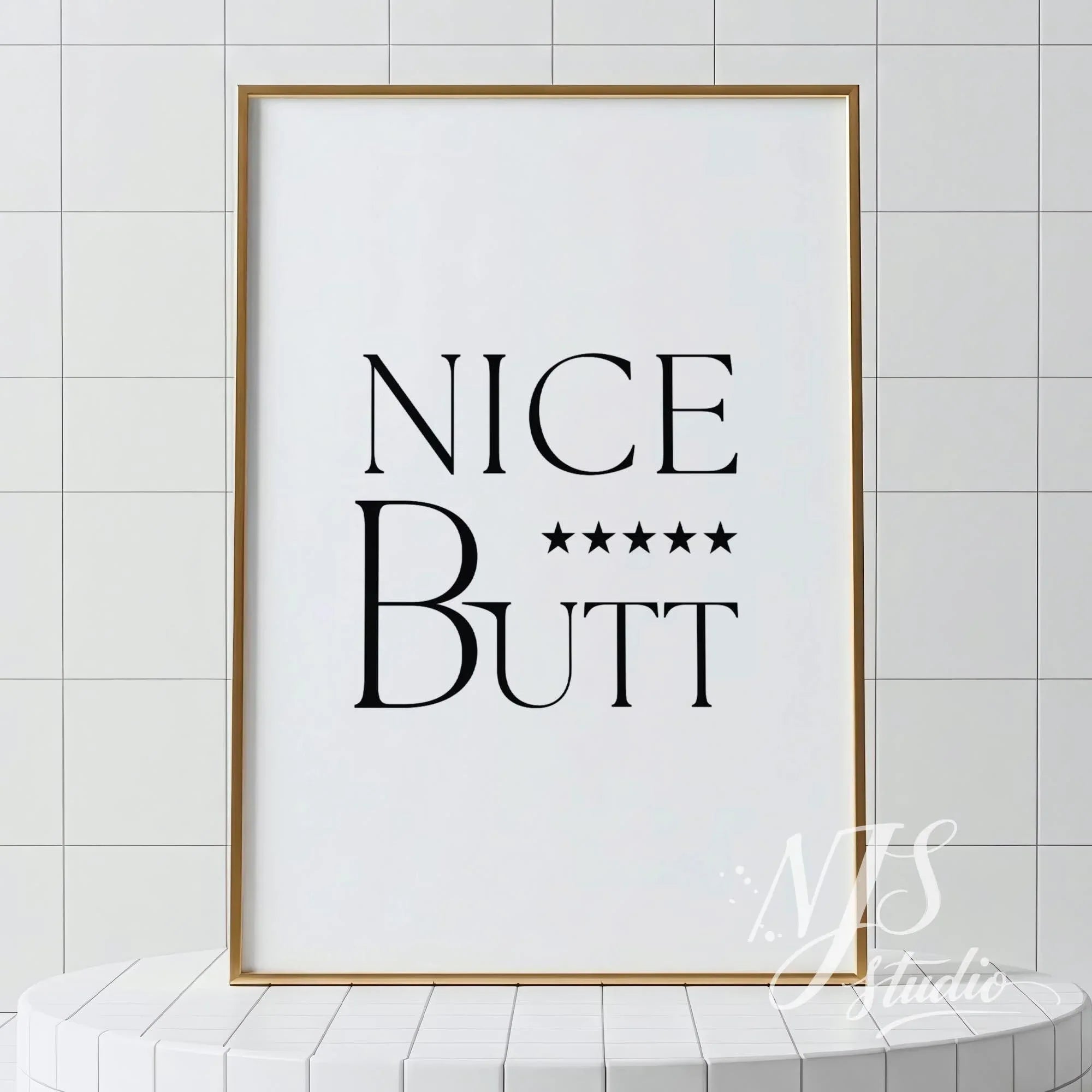 Minimal bathroom wall art featuring the text “Nice Butt” with five stars, displayed in a light wood frame against tiled walls.