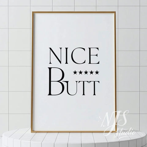 Minimal bathroom wall art featuring the text “Nice Butt” with five stars, displayed in a light wood frame against tiled walls.