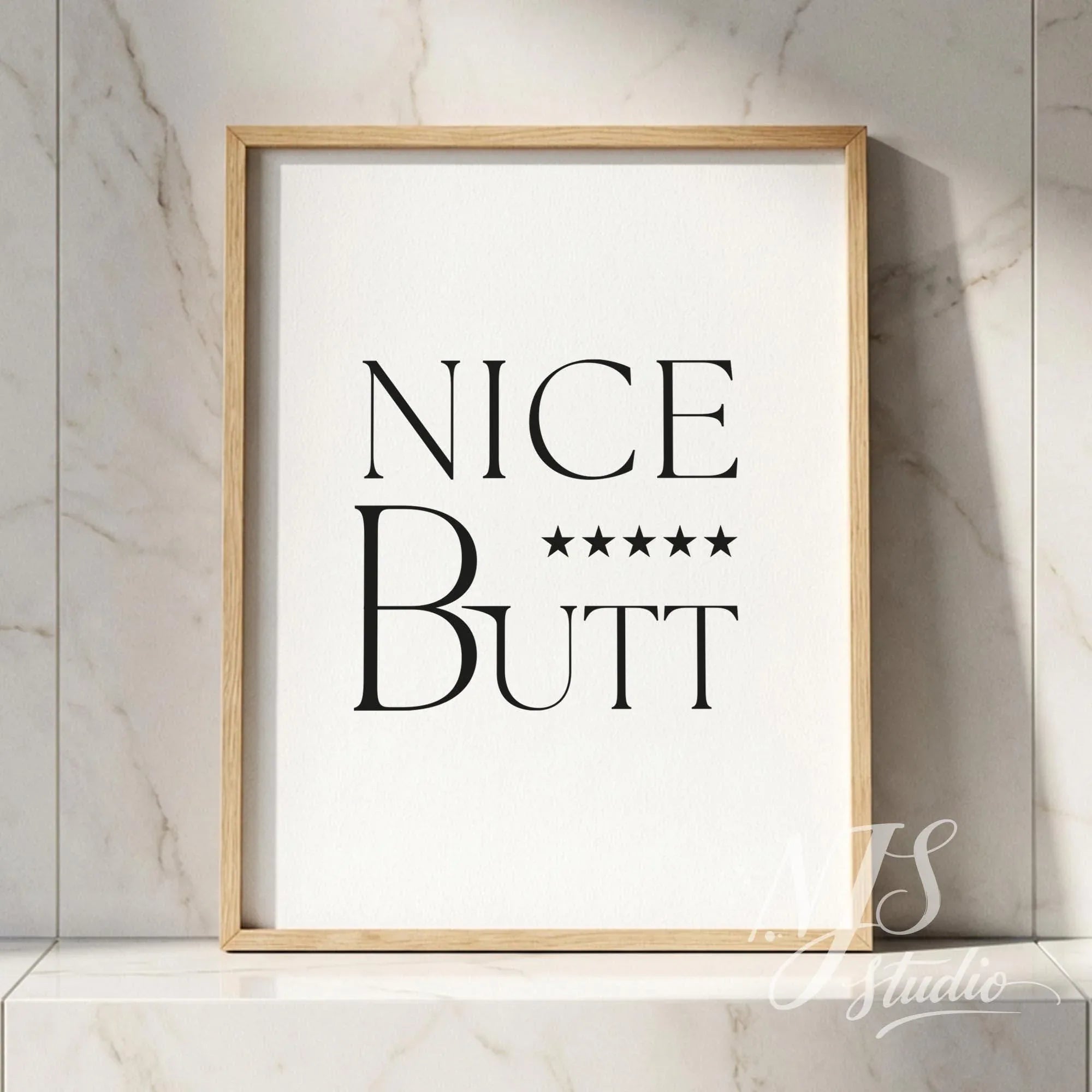 Typography bathroom poster with the phrase “Nice Butt” and five stars, framed in wood and placed against a marble tile wall.