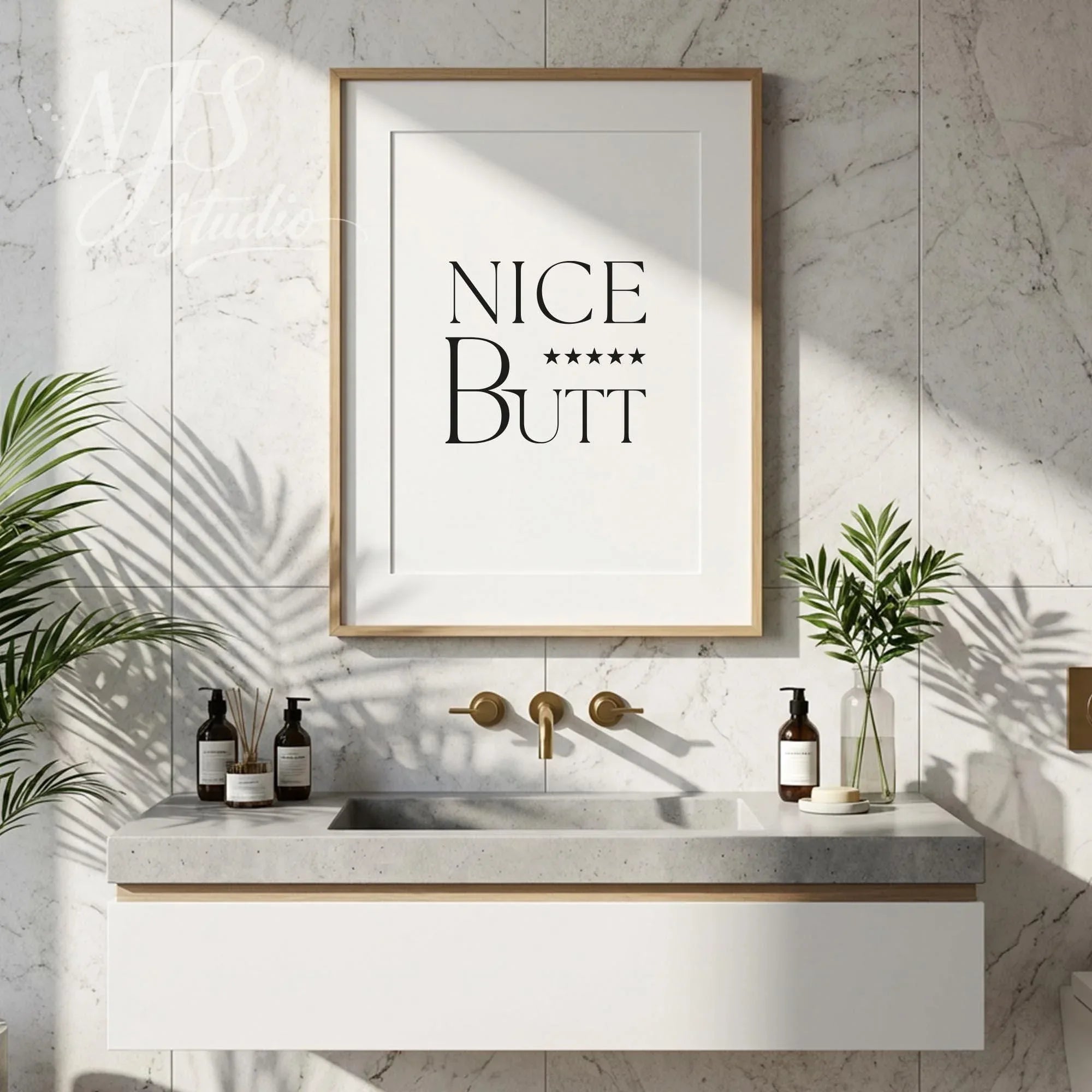 Funny bathroom wall art with the phrase “Nice Butt” displayed above a modern vanity with plants and soap bottles.