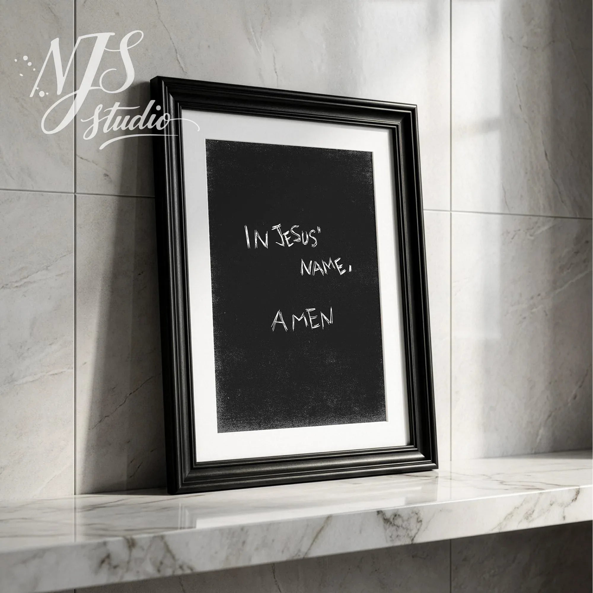 Black framed religious art print In Jesus Name Amen leaning on a marble shelf in a modern home.