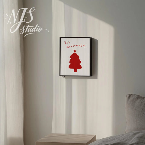 Black framed holiday print saying Its Christmas with a cute red tree graphic hanging on a white wall.