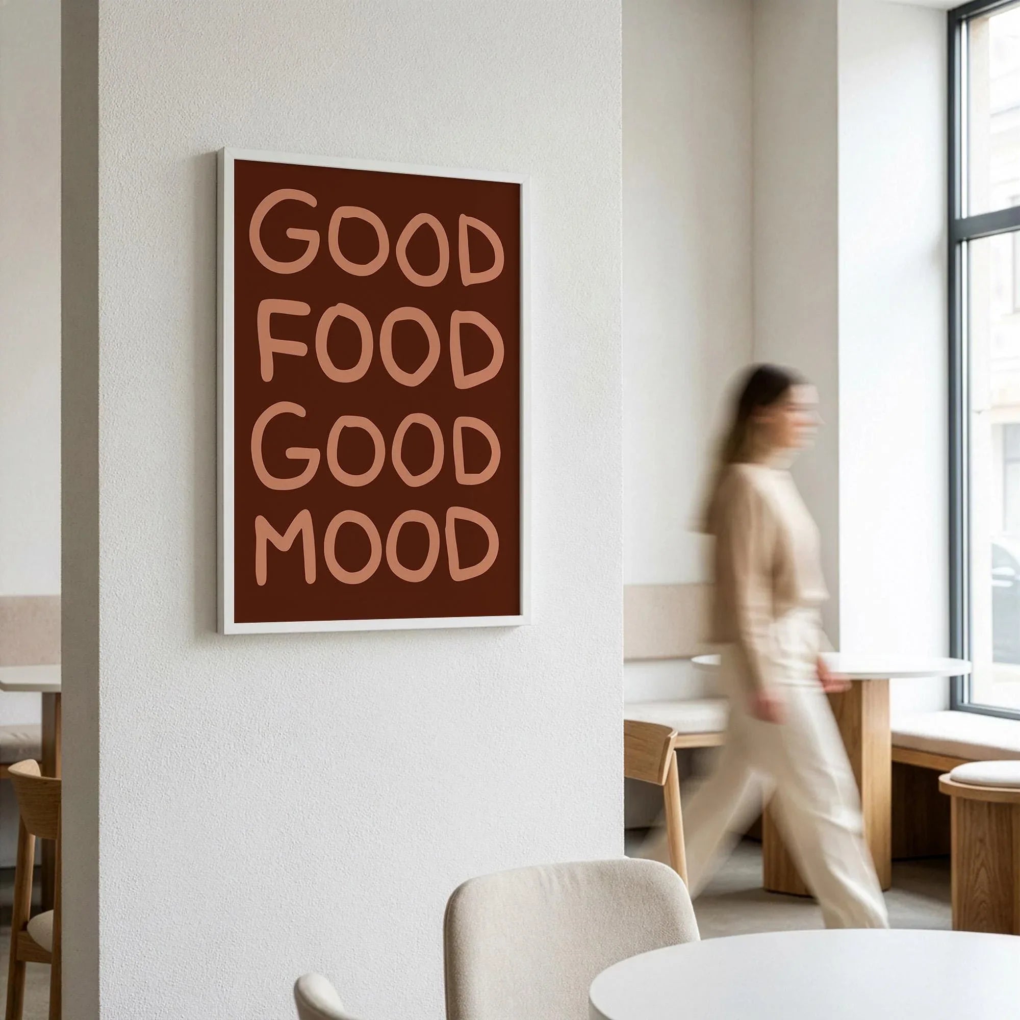 Wood framed brown Good Food Good Mood art print hanging on a white wall in a busy coffee shop.