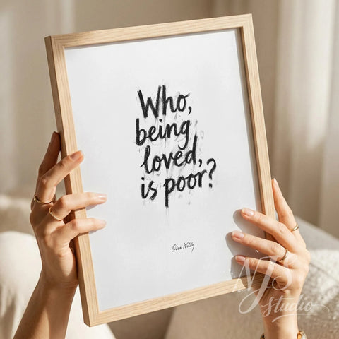 Hands holding a light wood framed print with bold brush lettering quote Who being loved is poor.