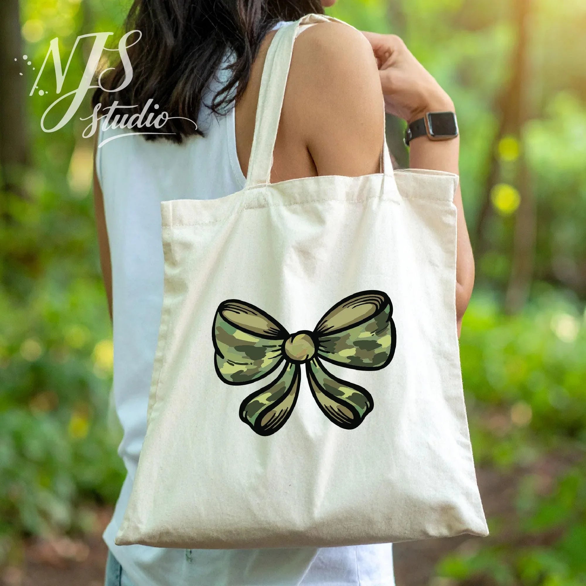 Natural canvas tote bag featuring a green camo bow graphic, carried outdoors in a leafy environment