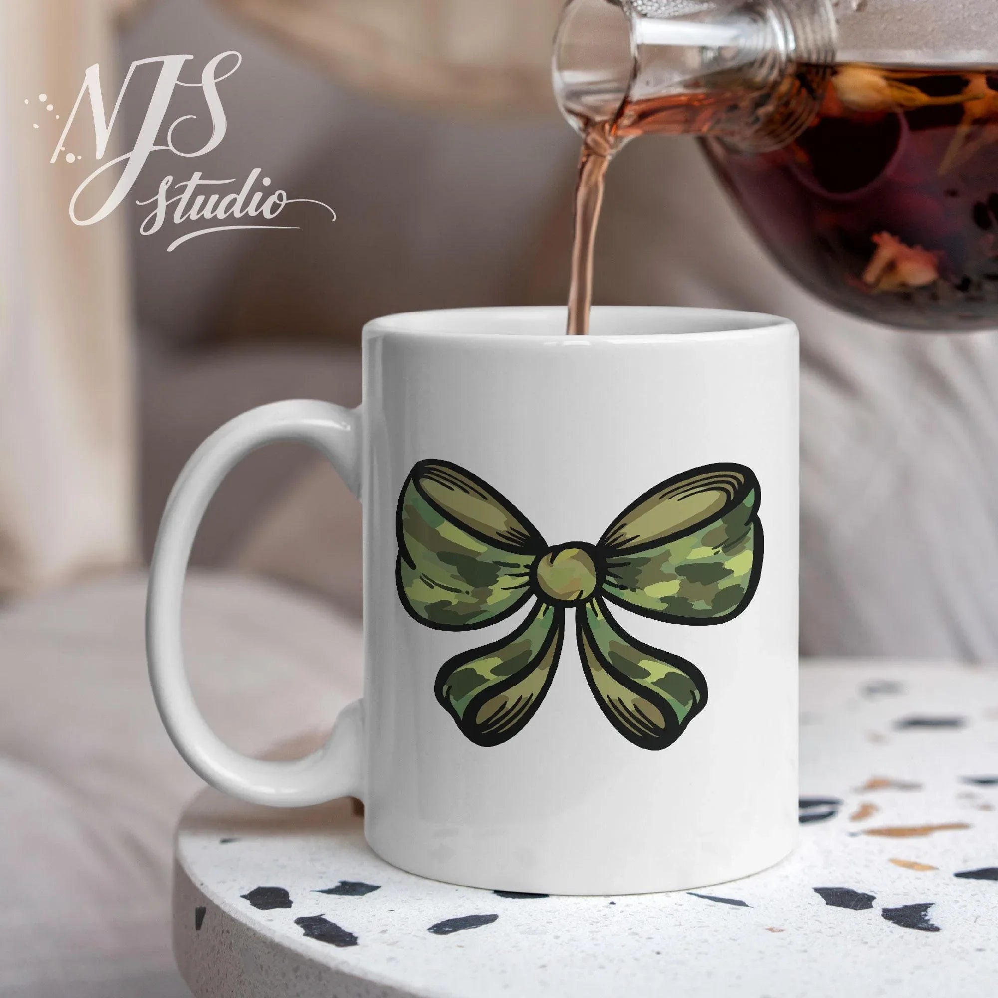 White ceramic mug with a camouflage bow design as tea is poured, styled on a cozy tabletop