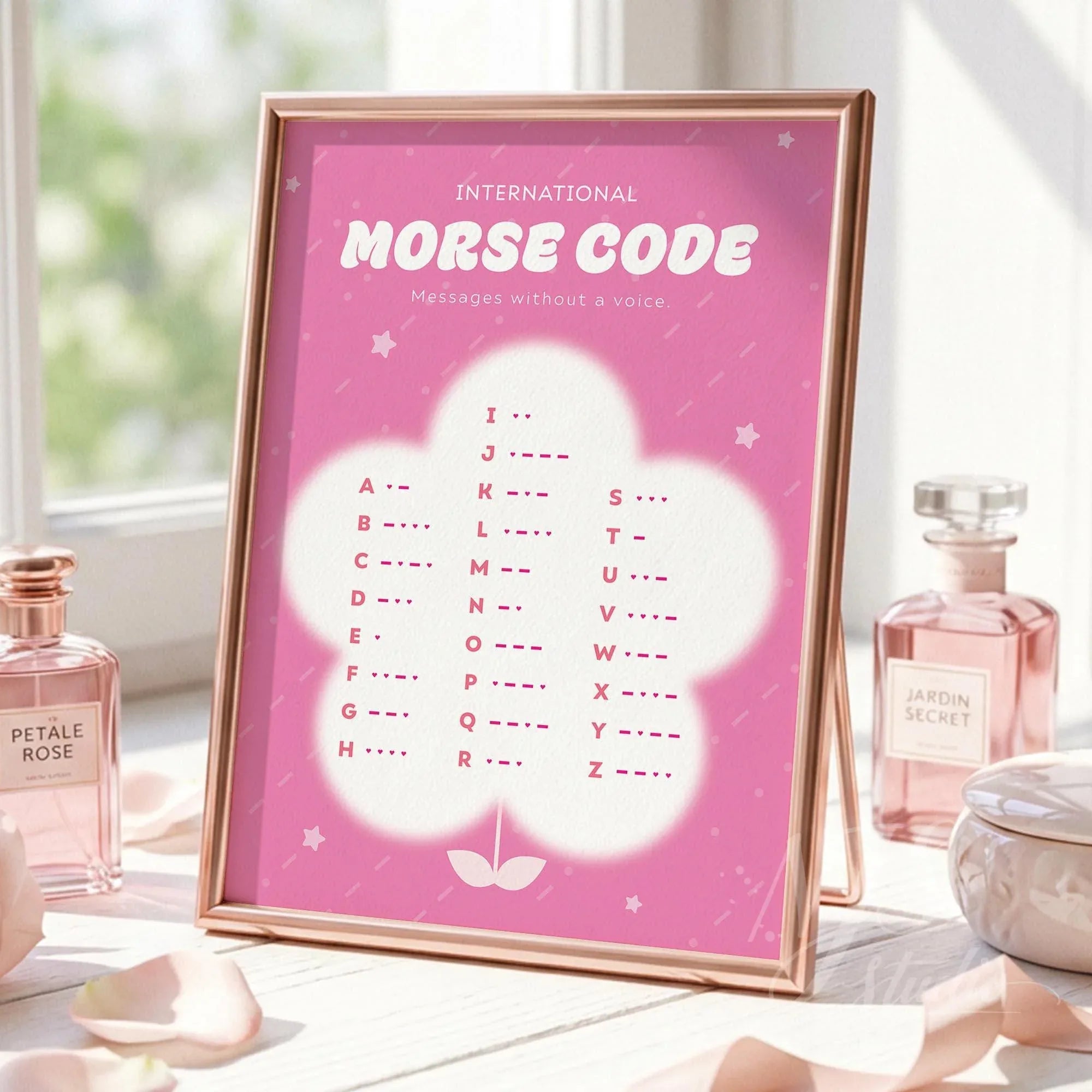 Rose gold framed pink Morse code art standing on a sunlit vanity table with perfume bottles and scattered rose petals.