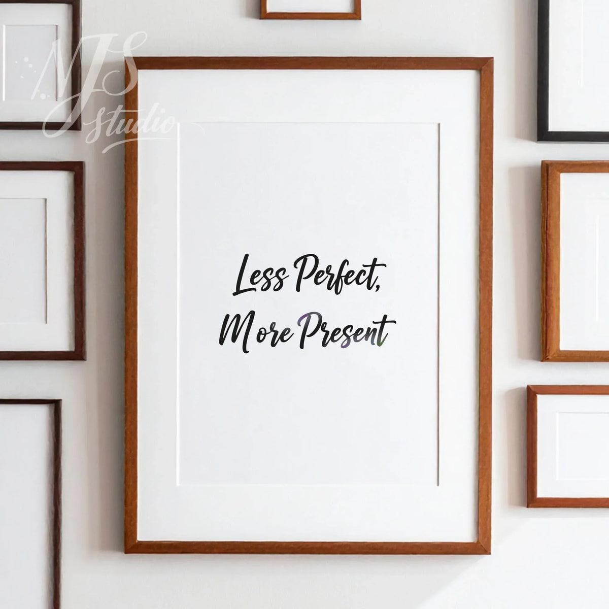Large framed "Less Perfect More Present" print hanging on a wall surrounded by several smaller art frames, stylish gallery wall decor.