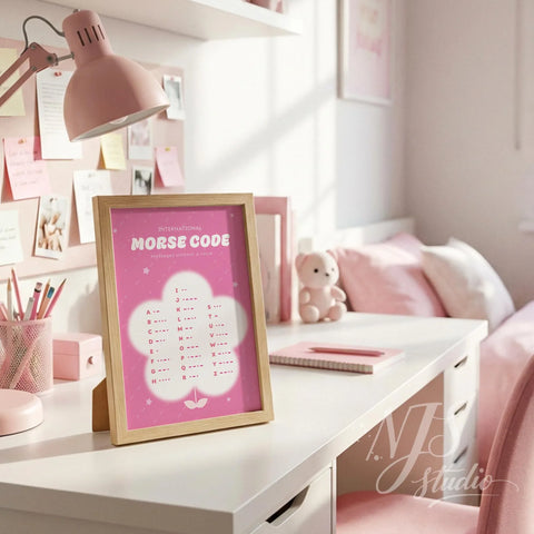 Wood framed pink Morse code chart standing on a white desk with pink stationery and lamp.