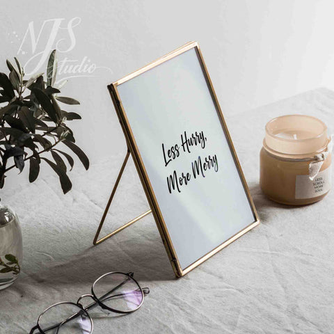 Elegant gold framed motivational print standing on a table with a candle and reading glasses.