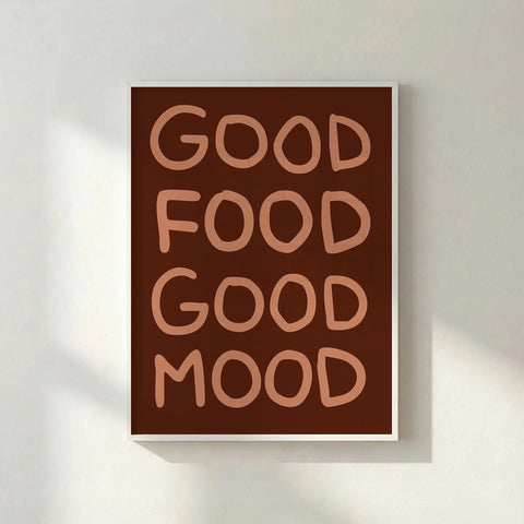 White framed brown typography poster saying Good Food Good Mood leaning against a white textured wall.
