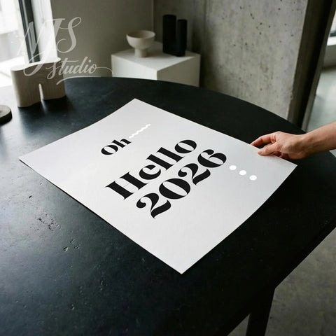 Hand holding modern 'Oh Hello 2026' print on black table, NJS studio creative workspace.