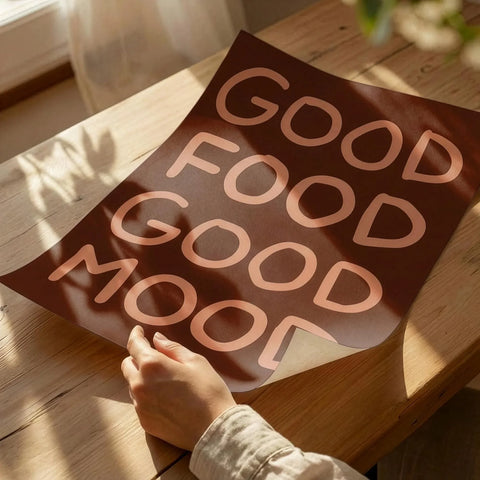 Hands unrolling a high quality brown art print with peach text Good Food Good Mood for kitchen decor.