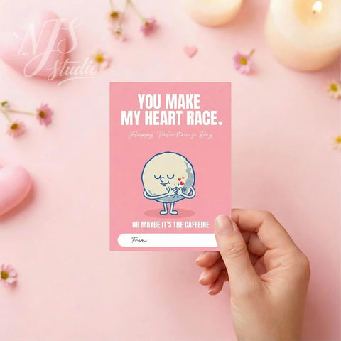 Hand holding pink Valentine card with cute caffeine-themed heart, NJS Studio branding, flowers, candles