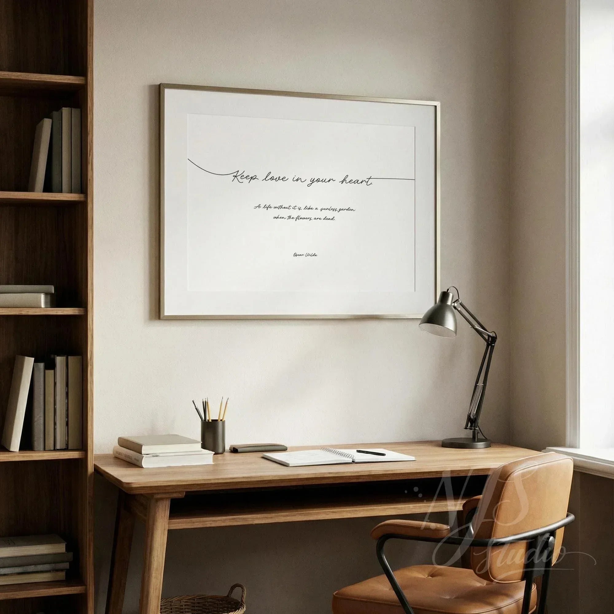 Minimalist framed wall art with flowing line script typography hanging above a wooden desk with lamp.