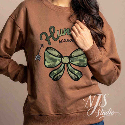 Brown sweatshirt with a green camo bow and hunting season graphic, modeled in a warm indoor setting.