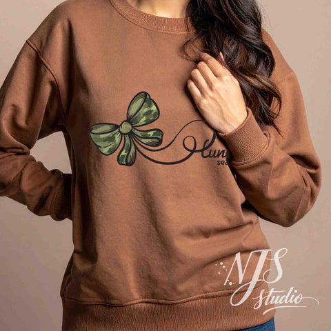 Brown sweatshirt with a green camo bow and elegant hunting season script, modeled indoors for a cozy fall apparel look.