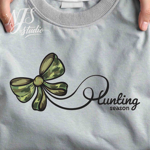 Folded gray sweatshirt featuring a green camouflage bow connected to a handwritten “Hunting Season” design, shown as a clean product mockup.