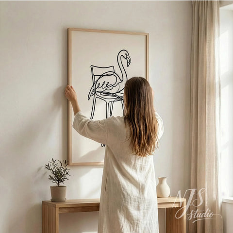 Woman hanging large flamingo line art poster with Off Duty text on wall, modern neutral home decor showing artwork size scale