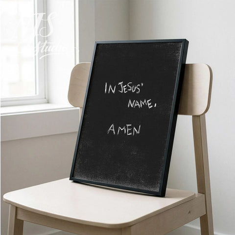 Simple black bible verse print leaning on a wooden chair in a bright minimalist room.