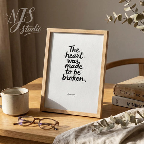 Wood framed literary quote standing on a desk with glasses and books, reading The heart was made to be broken.