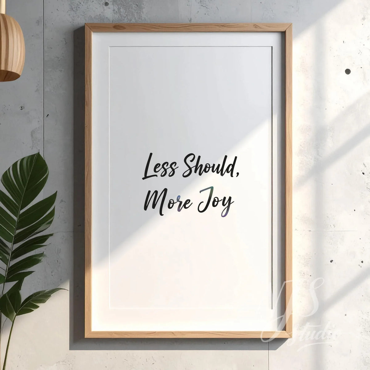 Wooden framed poster on a textured concrete wall, reading Less Should More Joy.