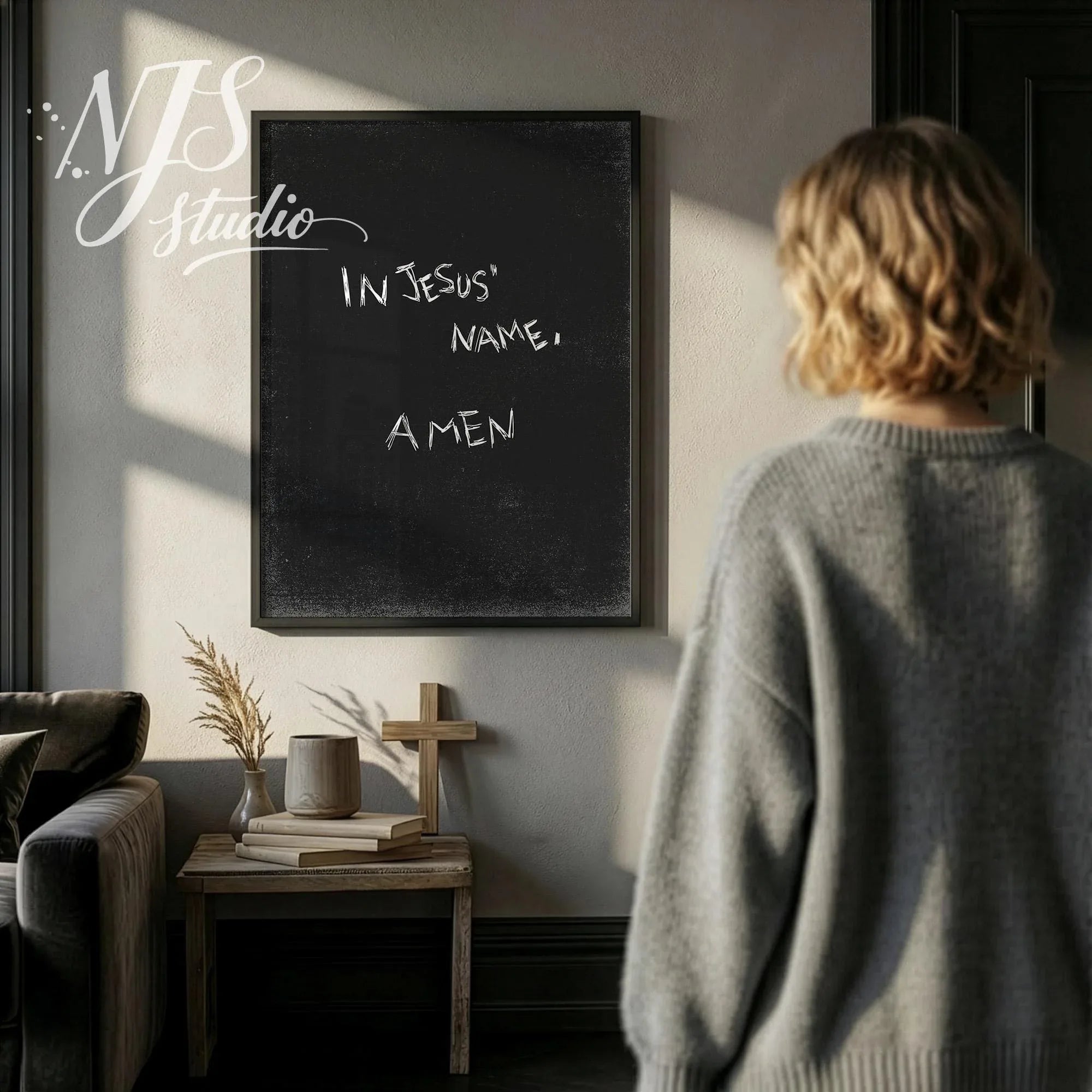 Woman standing in a moody dark grey room looking at a large framed In Jesus Name Amen poster.