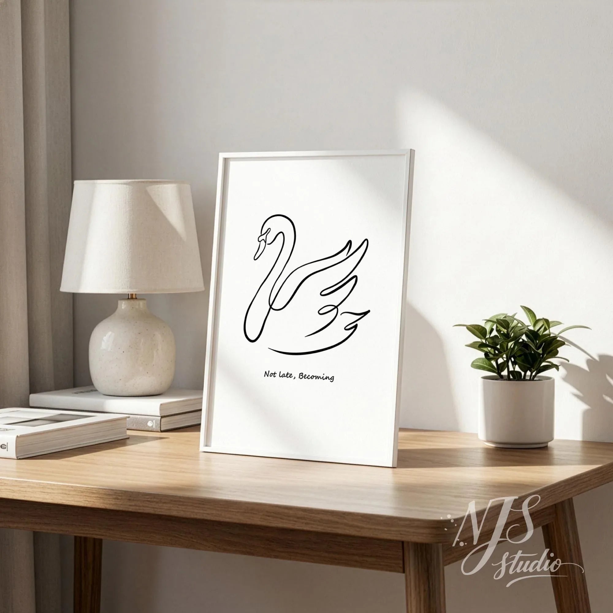 Framed swan line art wall print on wooden desk next to table lamp and small plant, soft natural light home decor scene