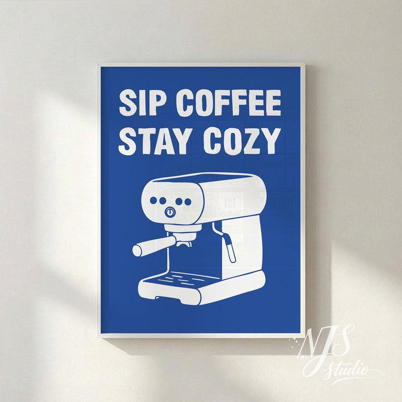 Framed poster with 'Sip Coffee Stay Cozy' text and an espresso machine illustration on a blue background.