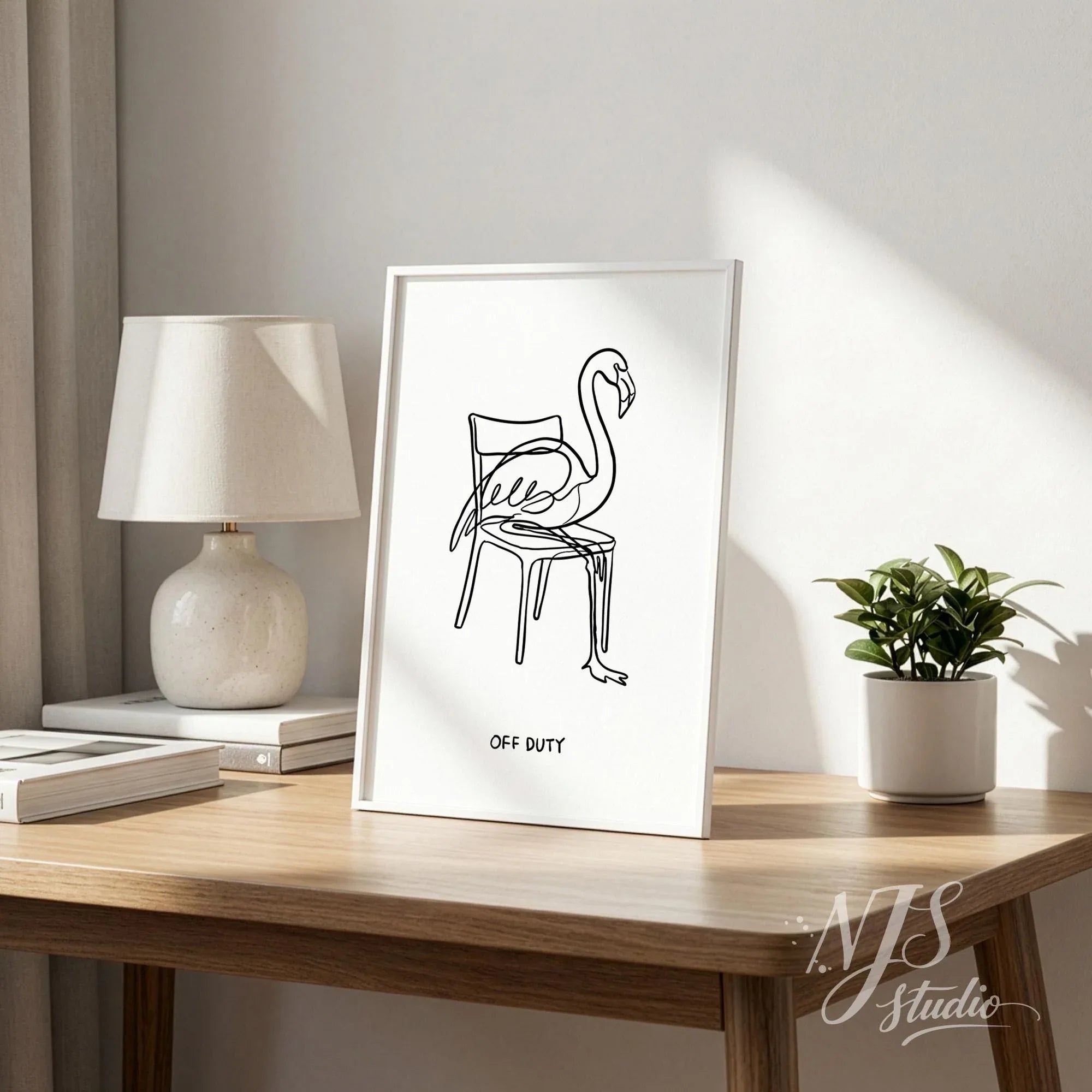 Small framed flamingo line art print with Off Duty quote on wooden desk, minimalist tabletop home decor in bright neutral interior