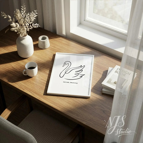 Minimal line art swan wall art in white frame placed on a wooden desk with coffee cup and dried flowers in soft morning sunlight.