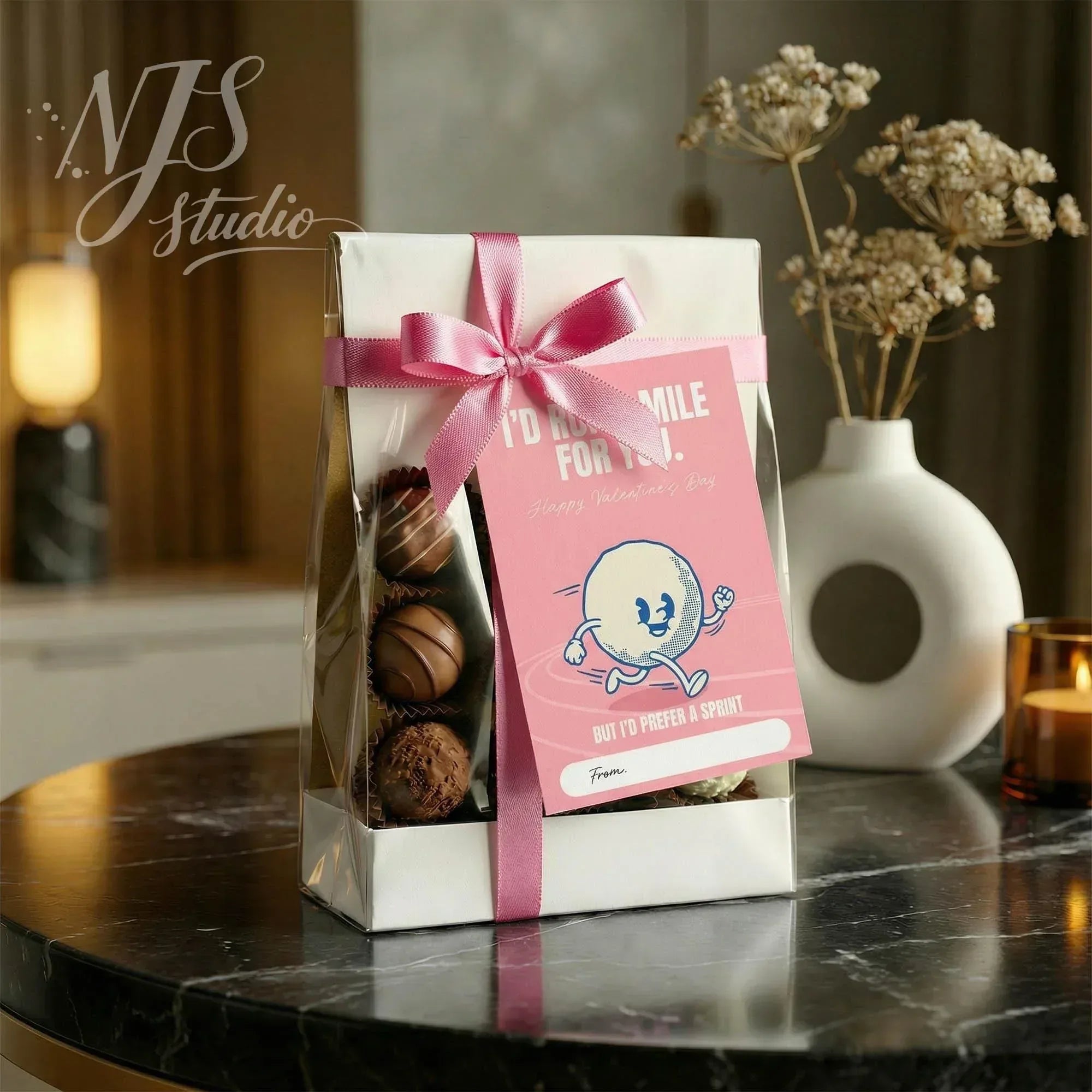 NJS studio Valentine gift box with assorted chocolates, pink ribbon, and card on marble table