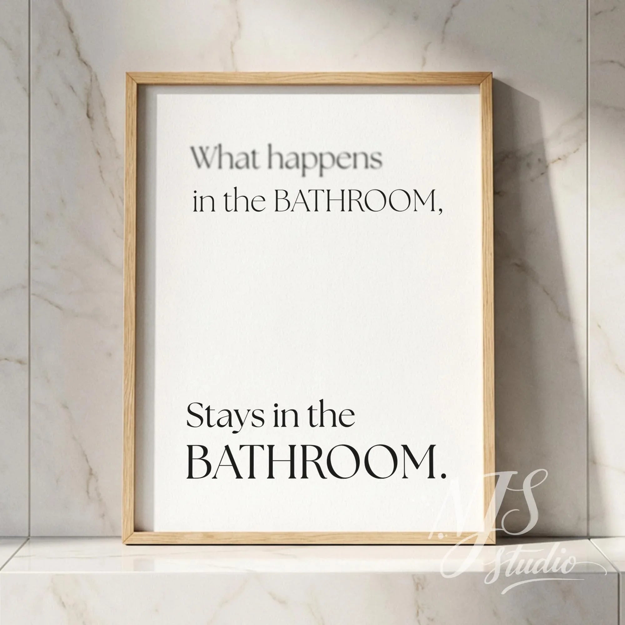 Minimal typography bathroom poster with the text “What happens in the bathroom, stays in the bathroom,” framed in natural wood against marble tiles.