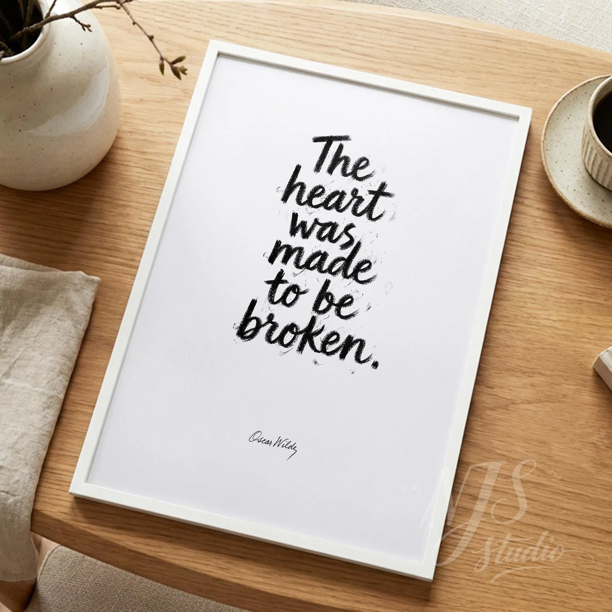 Minimalist white framed quote print standing on a wooden desk next to a white vase and ceramic cup, neutral home decor.