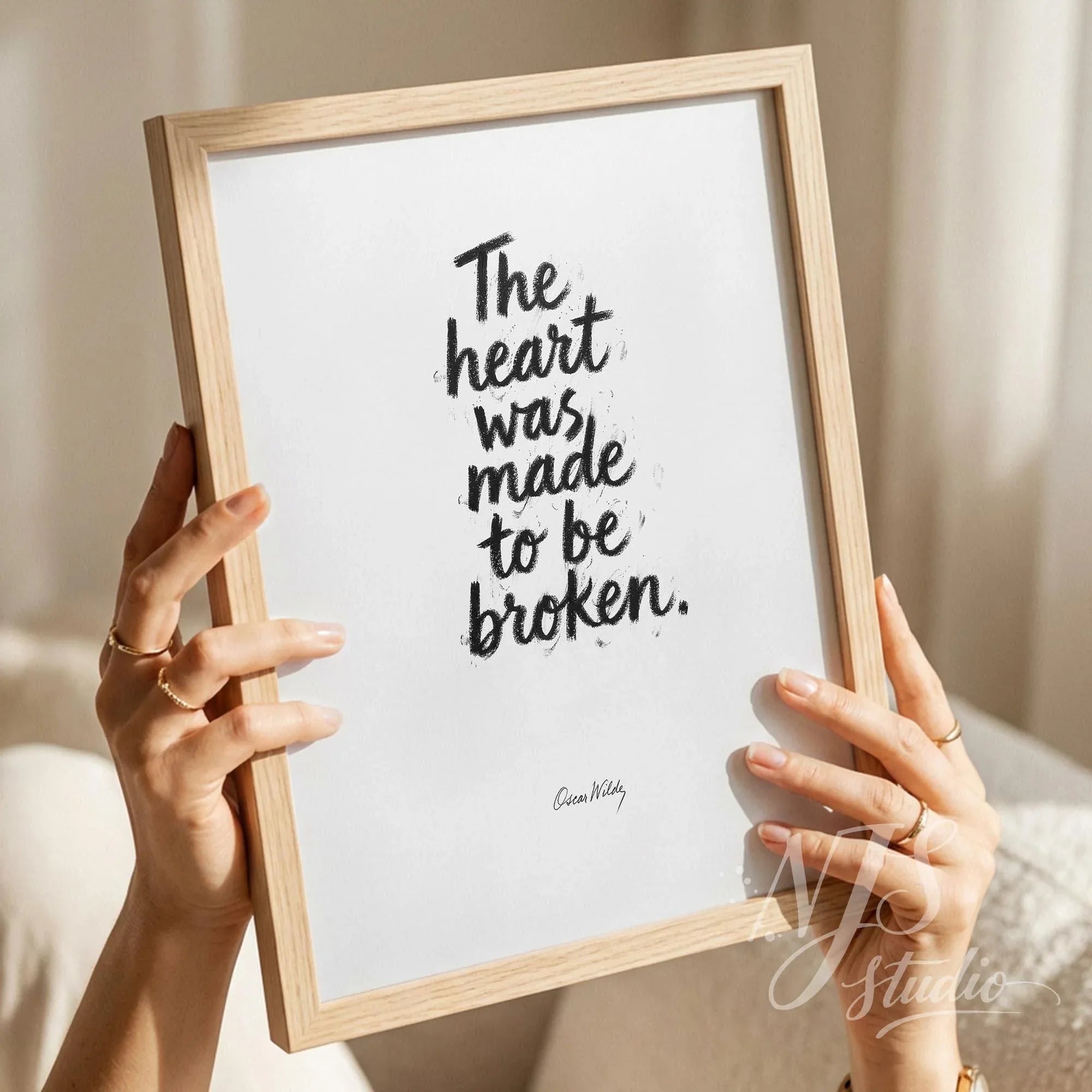 Woman holding a wooden framed print in front of her face, featuring Oscar Wilde's emotional quote.