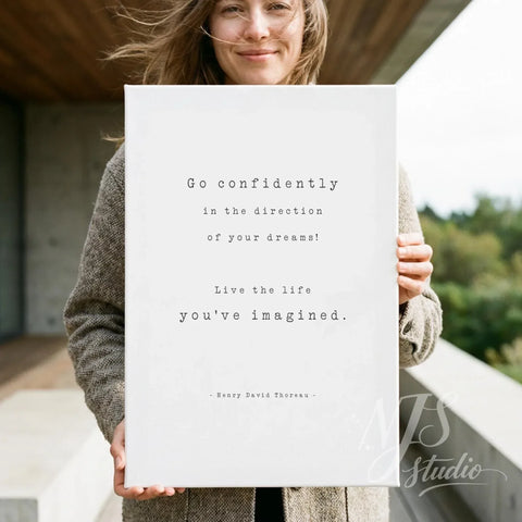 Woman holding a large white canvas print with the quote Go confidently in the direction of your dreams outdoors.